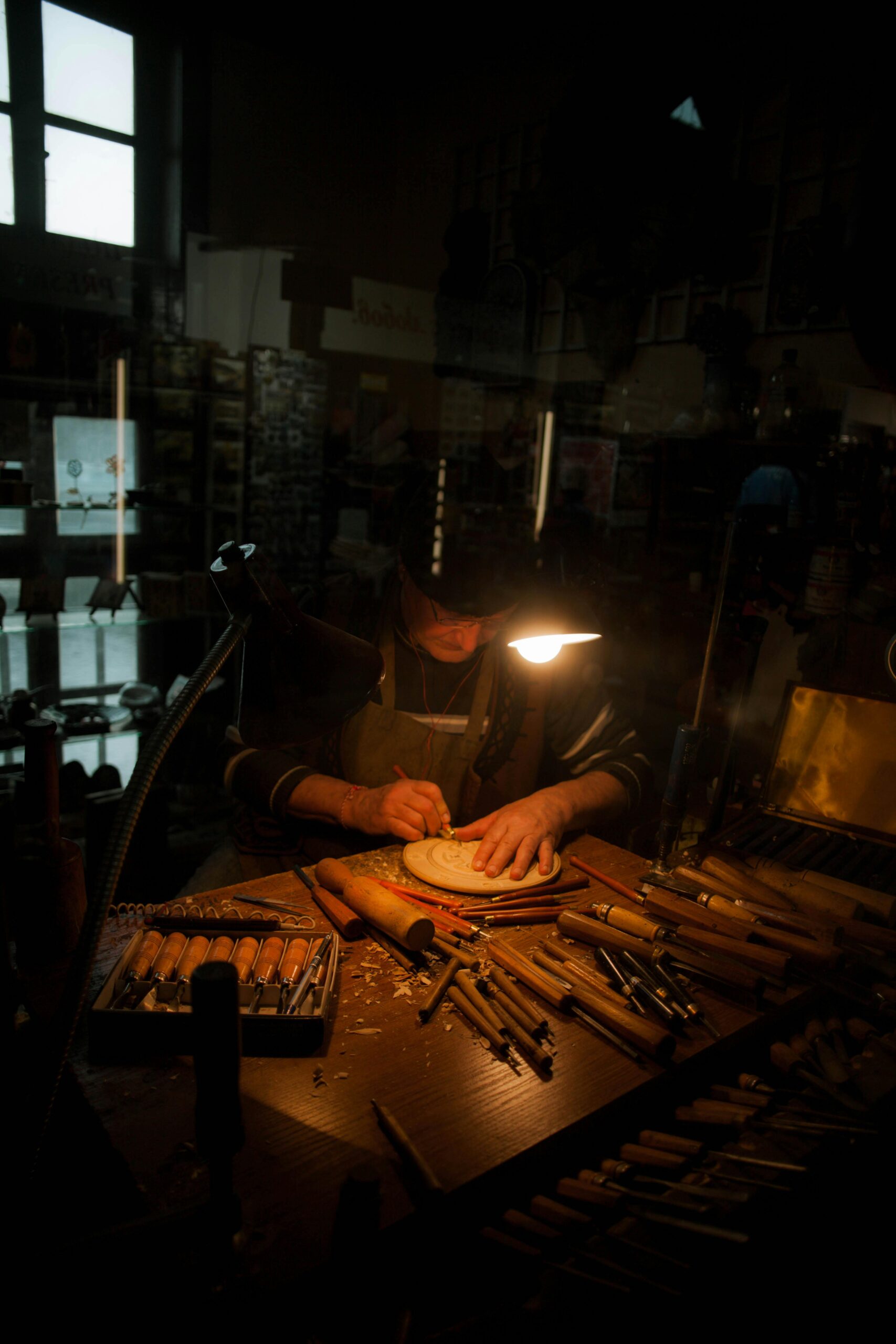 Artigianatoprime | Trova i migliori artigiani in tutta Italia Skilled craftsman wood carving under warm desk light, detailed tools visible on wooden table.