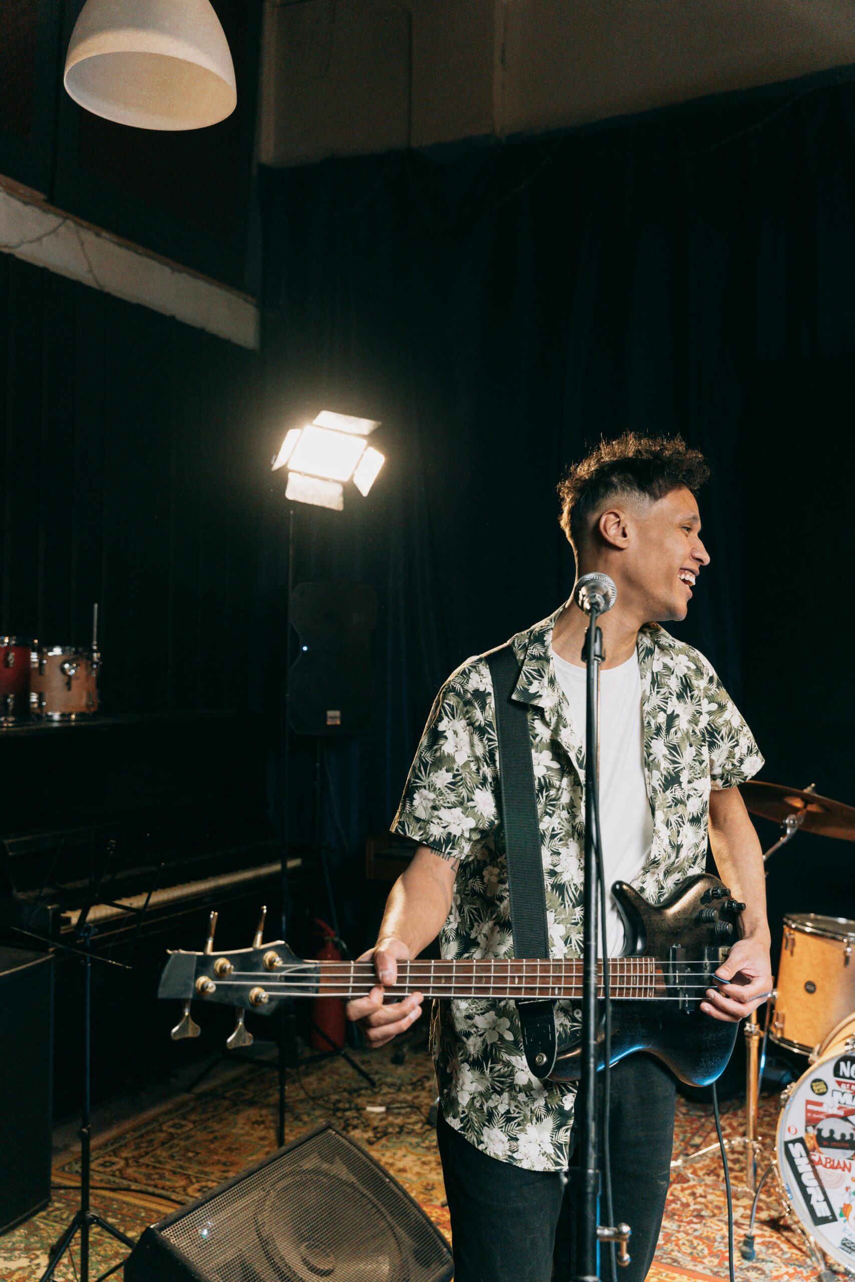 Musician smiling while performing on bass guitar in a cozy indoor setting with warm lighting.
